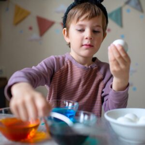 Cute child coloring Easter egg at home in springtime